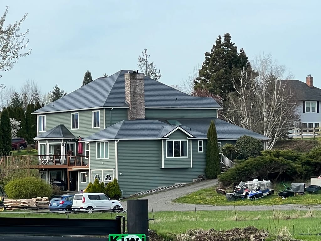 Deep Charcoal Interlock Slate aluminum roof on a two-storey home with a metal roof among tall trees, Enumclaw, Washington