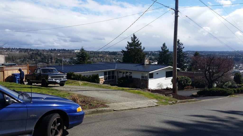 Black Interlock Standing Seam aluminum roof on a white single-family home with a metal roof among trees, Des Moines, Washington