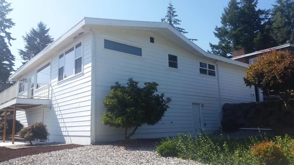 Before: the old roof on a white ranch-style home with a metal roof among trees, Des Moines, Washington, ahead of a Black Interlock Standing Seam aluminum roof