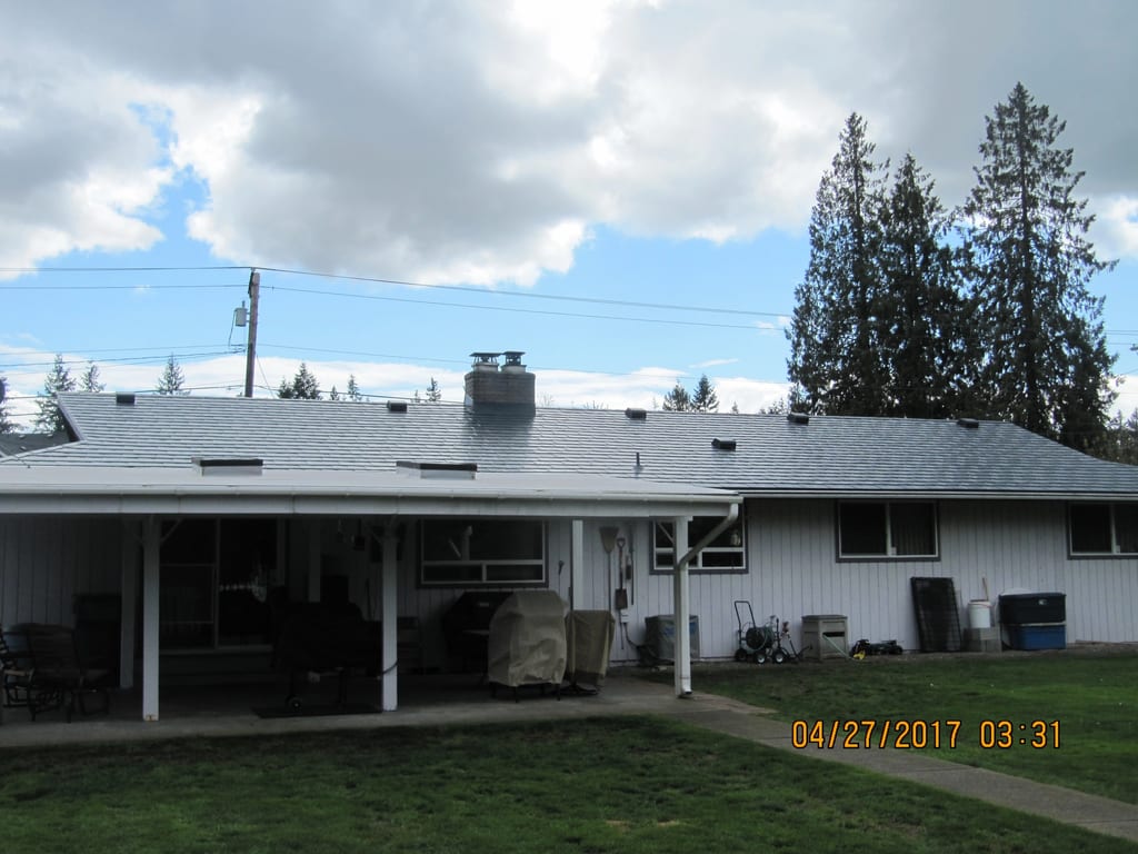Deep Charcoal Interlock Slate aluminum roof on a white ranch home with a metal roof among tall evergreen, Marysville, Washington