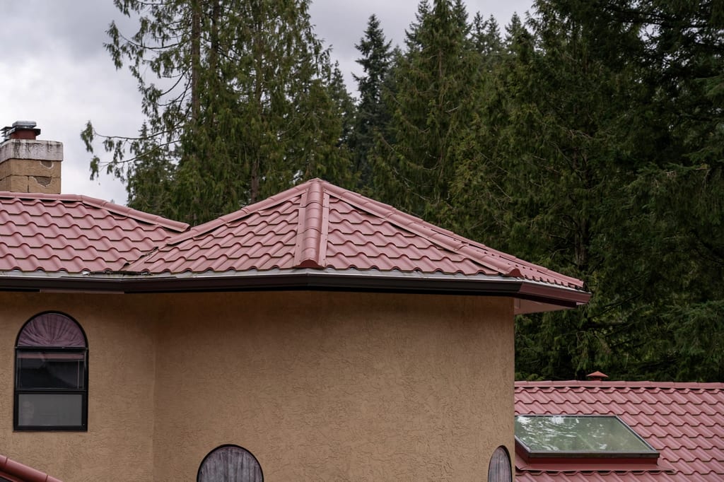 Tile Red Interlock Tile aluminum roof on a tan house with a red roof among tall trees in the forest, Woodinville, Washington