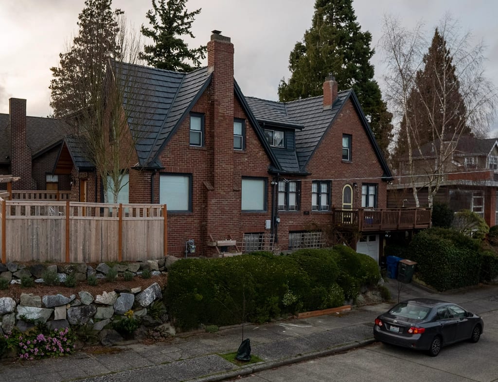 Deep Charcoal Interlock Shake aluminum roof on a brown two-storey Tudor home with dormers among trees, Seattle, Washington