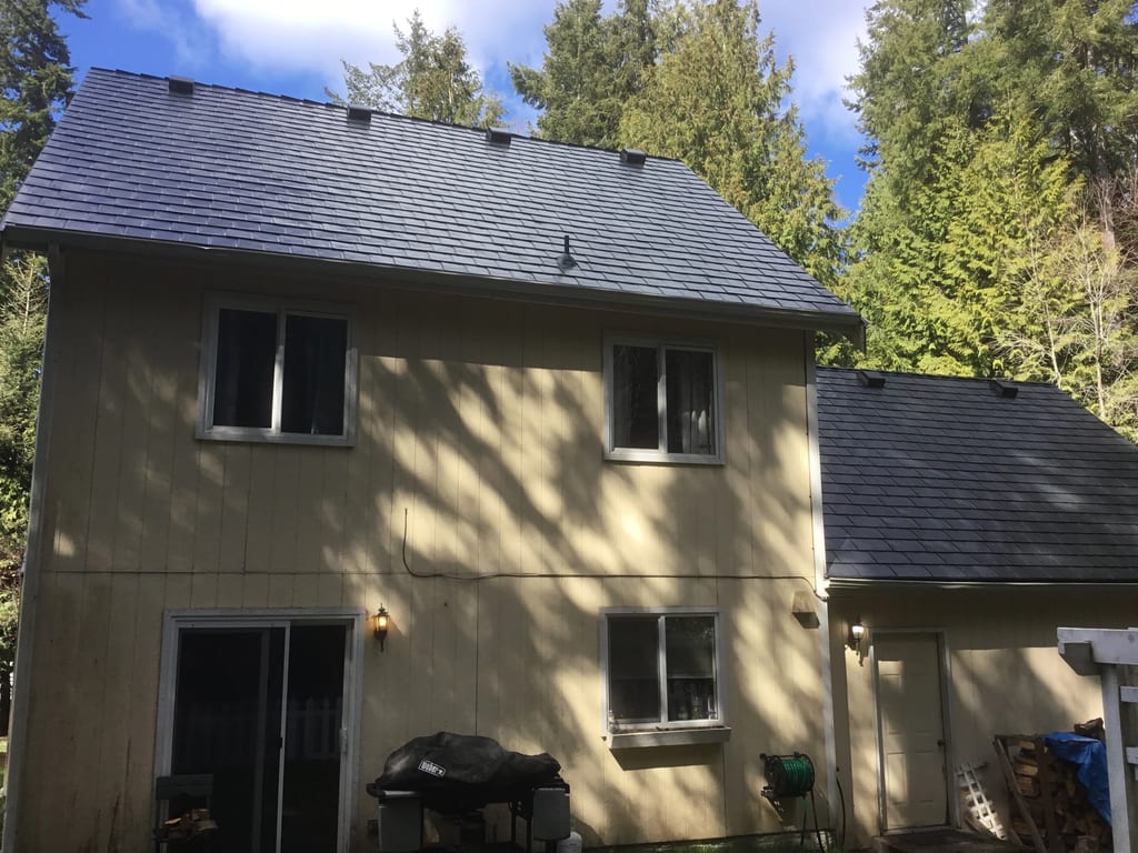 Black Interlock Slate aluminum roof on a two-storey home with a black metal roof among tall trees, Poulsbo, Washington