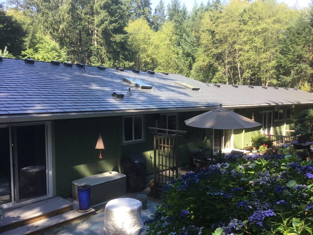 Deep Charcoal Interlock Slate aluminum roof on a two-storey green home with a metal roof in a forested area, Poulsbo, Washington