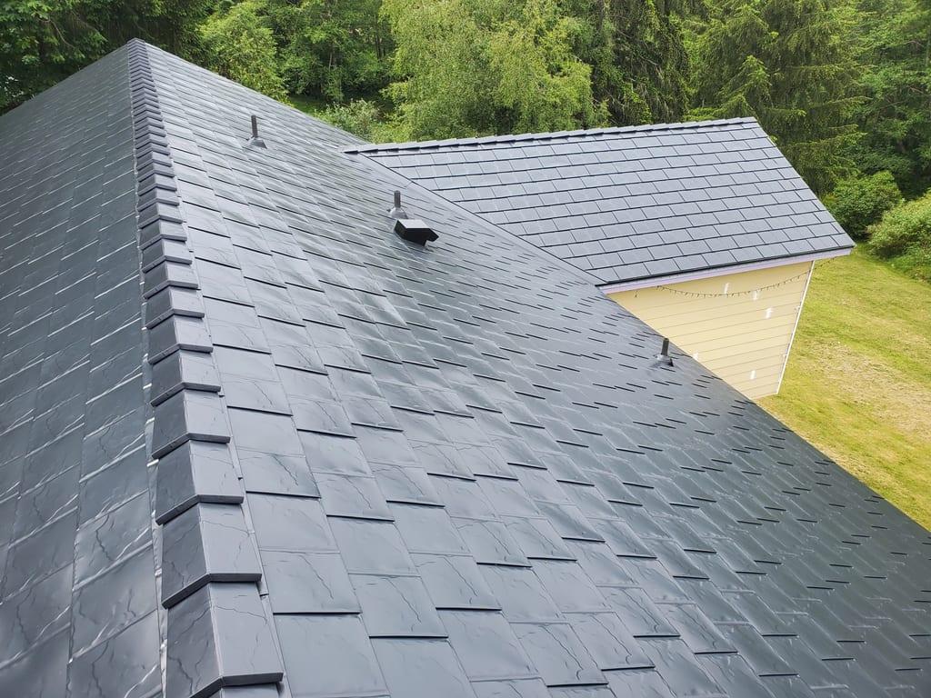 Black Interlock Slate aluminum roof on a dark two-storey home with dormers among tall conifers, Bremerton, Washington