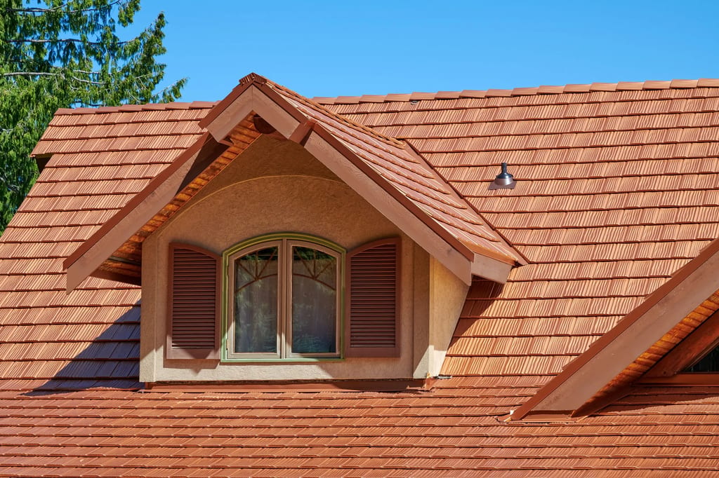 Close-up of a Copper Penny Interlock aluminum shake metal roof on a Craftsman-style home featuring a gabled dormer with arched window and wood shutters.