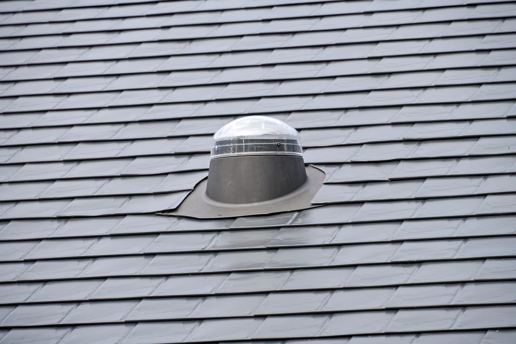 Close-up of a solar tube dome skylight with lead flashing installed on a dark grey Interlock aluminum slate metal roof.
