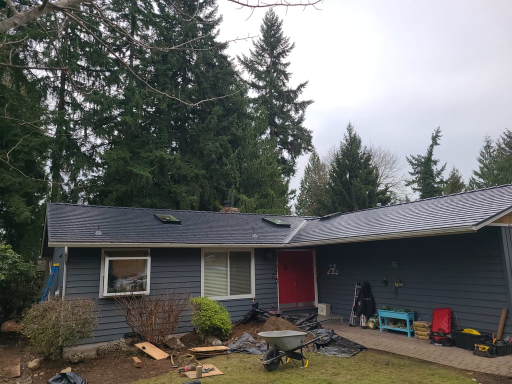 Front elevation of a gray ranch home with a newly installed Interlock black aluminum slate metal roof, skylights, and red front door in Redmond, WA.