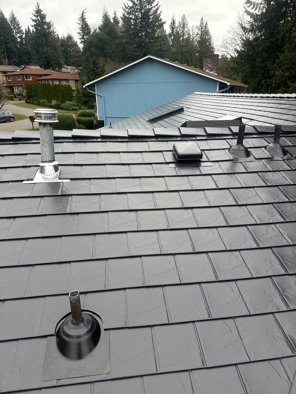Black Interlock Slate aluminum roof on a red one-storey home with a gable and dormers in a forest, Redmond, Washington
