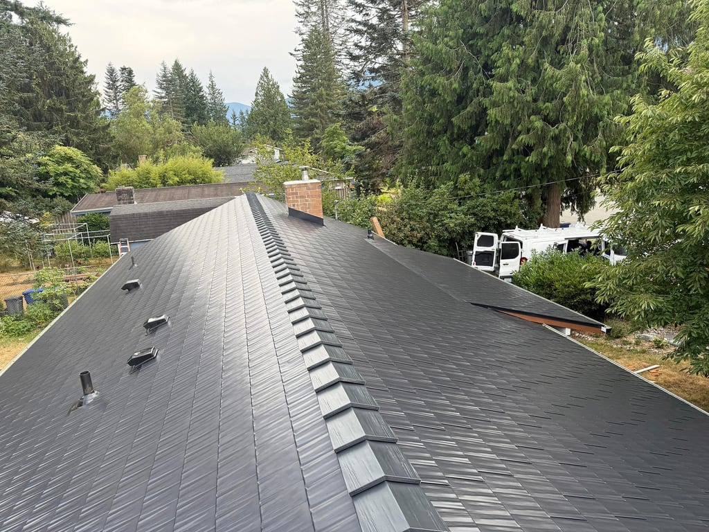 Black Interlock Cedar Shingle aluminum roof on a black two-storey home with a metal roof among tall pines, North Bend, Washington