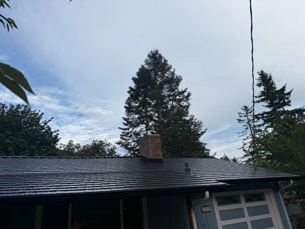 Black Interlock Cedar Shingle aluminum roof on a blue single-family home with dormers among tall pines, North Bend, Washington