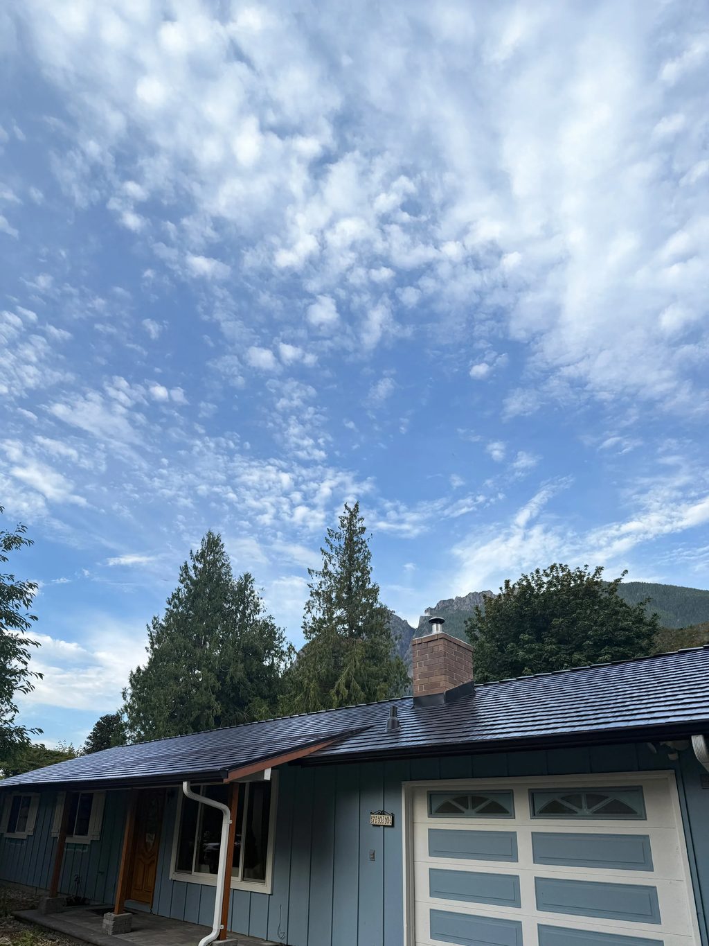 Black Interlock Cedar Shingle aluminum roof on a blue single-family home with a garage door in a forested, North Bend, Washington