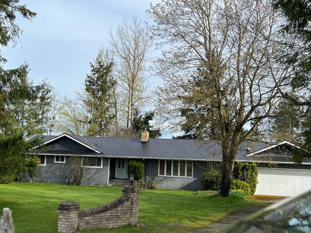 Black Interlock Slate aluminum roof on a grey ranch-style home with a metal roof among tall trees, Enumclaw, Washington