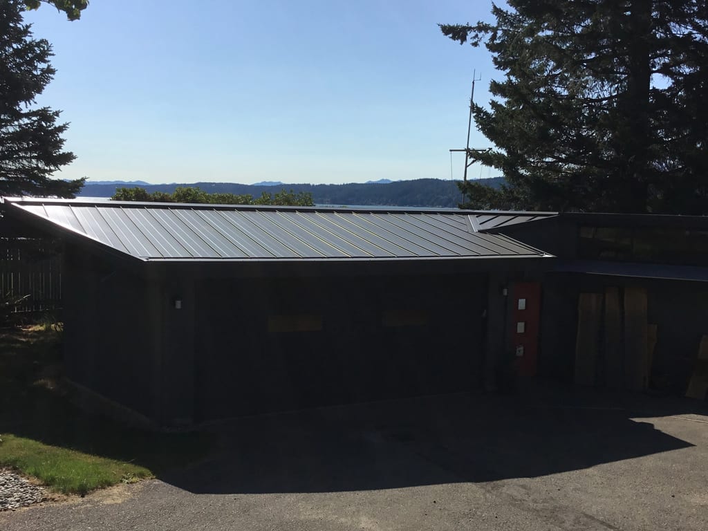Musket Grey Interlock Standing Seam aluminum roof on a grey two-storey home with dormers among tall pines, Belfair, Washington