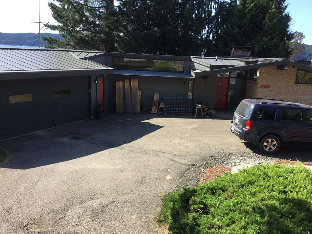 Musket Grey Interlock Standing Seam aluminum roof on a two-storey modern home with a metal roof among tall pines, Belfair, Washington