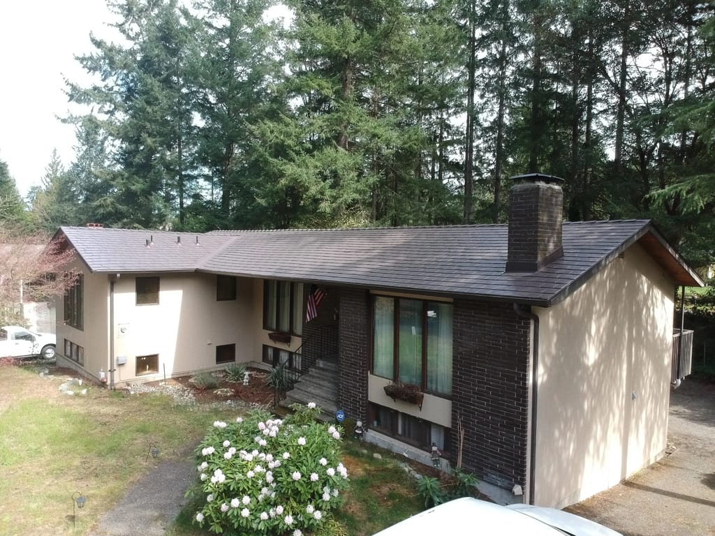 Tudor Brown Interlock Slate aluminum roof on a brown one-storey ranch home with brick accents among tall, University Place, Washington