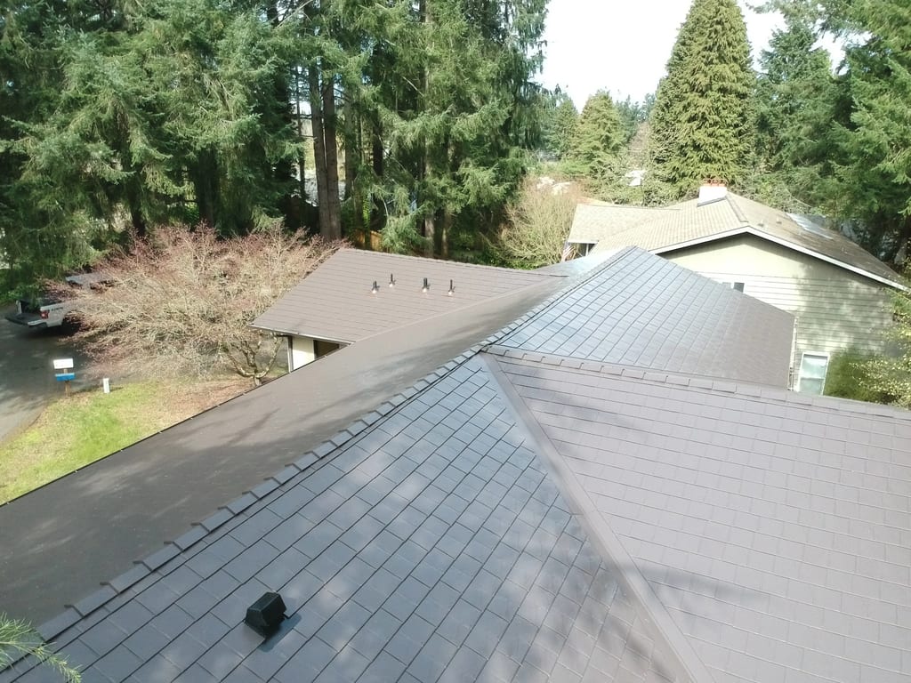 Tudor Brown Interlock Slate aluminum roof on a two-storey home with a metal roof among tall evergreen, University Place, Washington