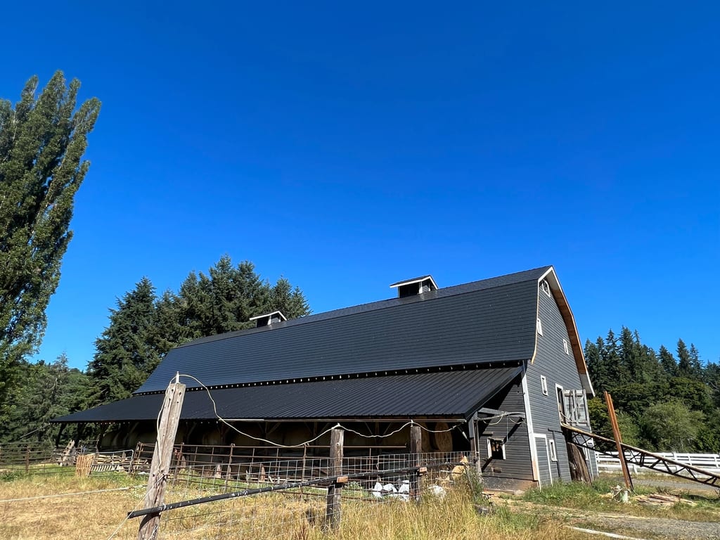 Black Interlock Slate aluminum roof on a black two-storey home with dormers among tall pines, Longview, Washington
