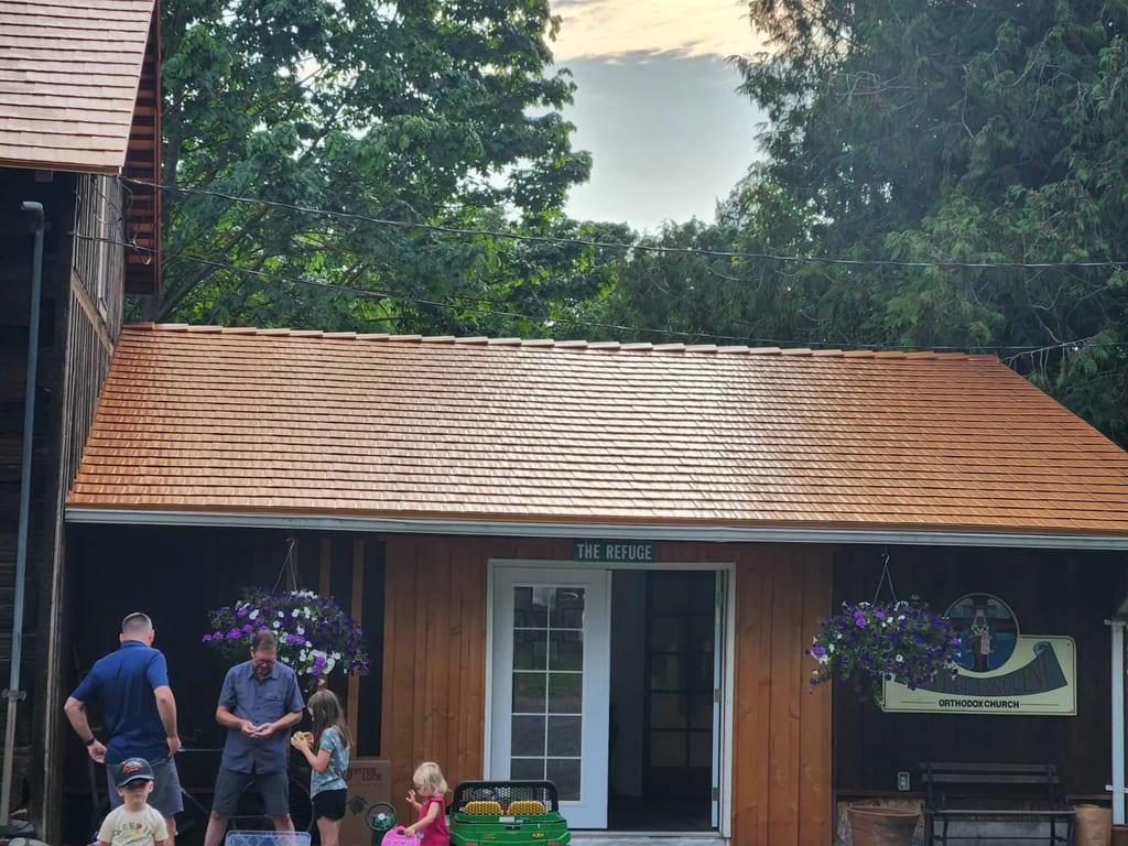Copper Penny Interlock Cedar Shingle aluminum roof being installed on a wood-sided home with a brown roof and green trees, Everson, Washington
