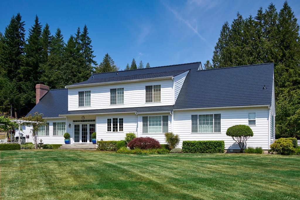 Black Interlock Slate aluminum roof on a white two-storey home with dormers among tall evergreens, Enumclaw, Washington