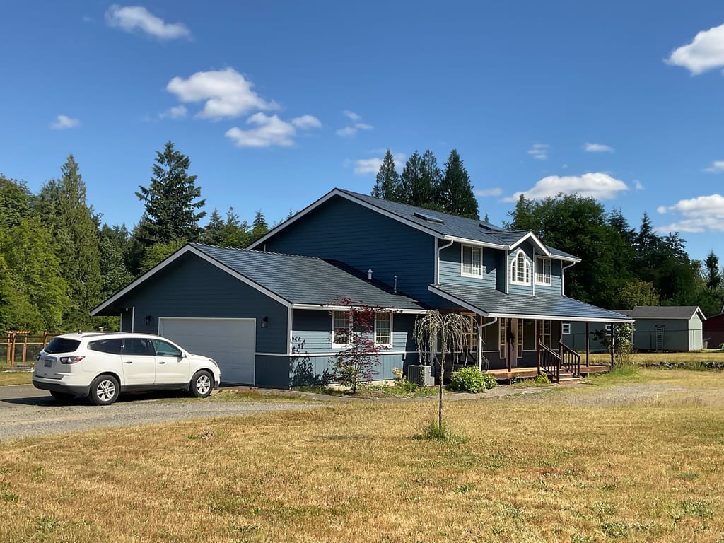 Two-story Craftsman home with Interlock deep charcoal cedar shingle metal roof, covered front porch, attached garage, set on a rural forested acreage in Olympia, WA.
