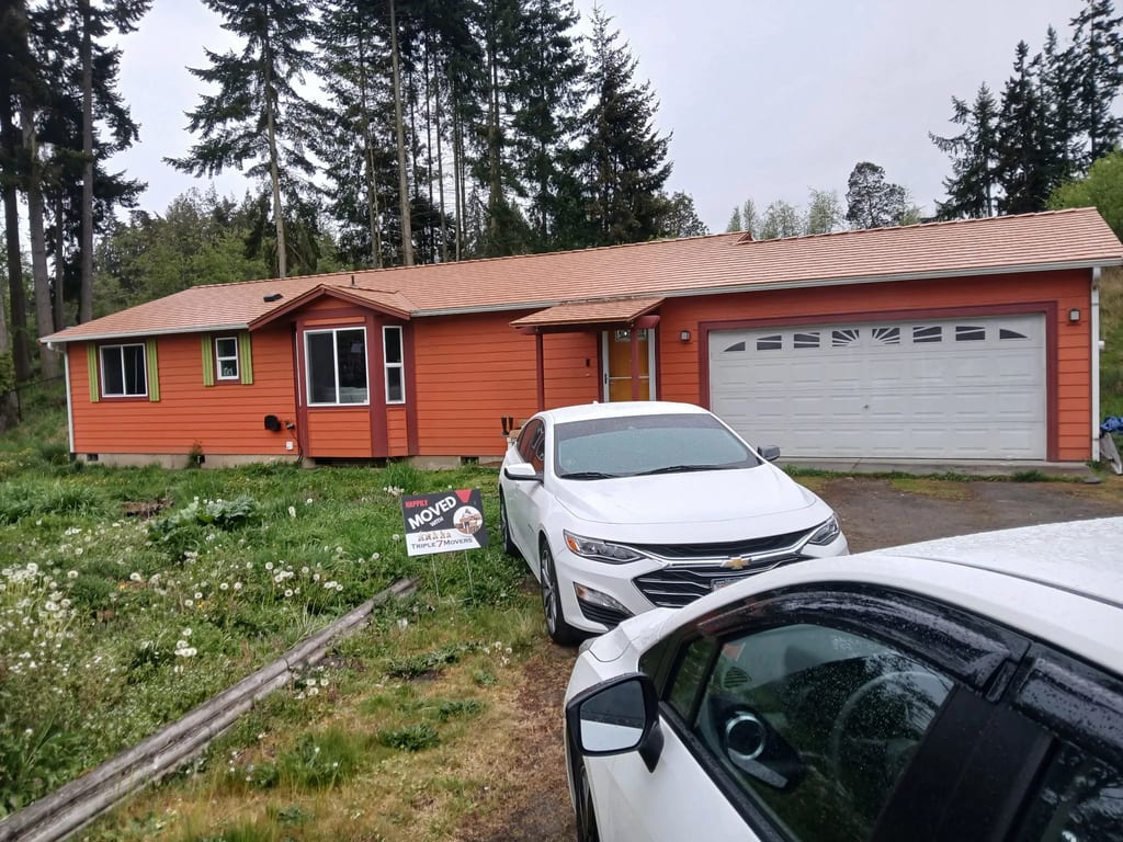 Copper Penny Interlock Slate aluminum roof on a red one-storey home with a garage and dormers among tall, Sequim, Washington