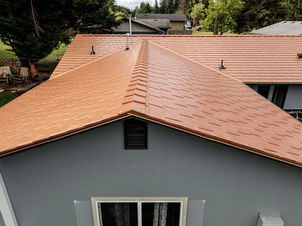 Copper Penny Interlock Slate aluminum roof on a grey one-storey home with a copper roof among tall trees, Castle Rock, Washington