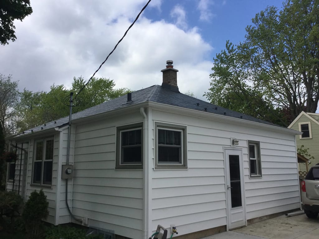 Charcoal Grey Interlock Slate aluminum roof on a white single-storey home with a metal roof among tall, Madison, Wisconsin