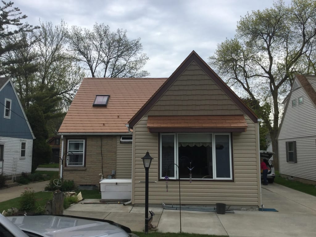 Aged Copper Interlock Slate aluminum roof on a beige cottage with a metal roof and brown trim among tall, Milwaukee, Wisconsin
