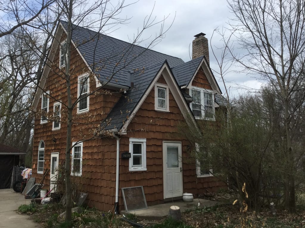 Black Interlock Slate aluminum roof on a brown house with white trim and a black roof in a forest, Madison, Wisconsin