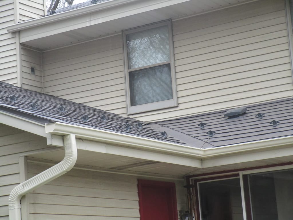 Tudor Brown Interlock Slate aluminum roof on a cream two-storey home with dormers among tall trees, Delafield, Wisconsin