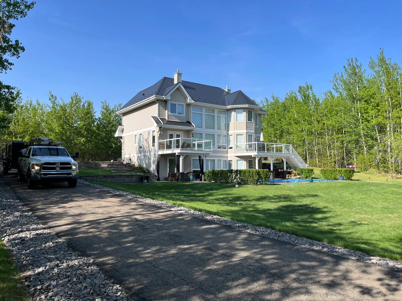 Black Interlock Cedar Shingle aluminum roof on a beige two-storey home with dormers among tall pines, Sherwood Park, Alberta