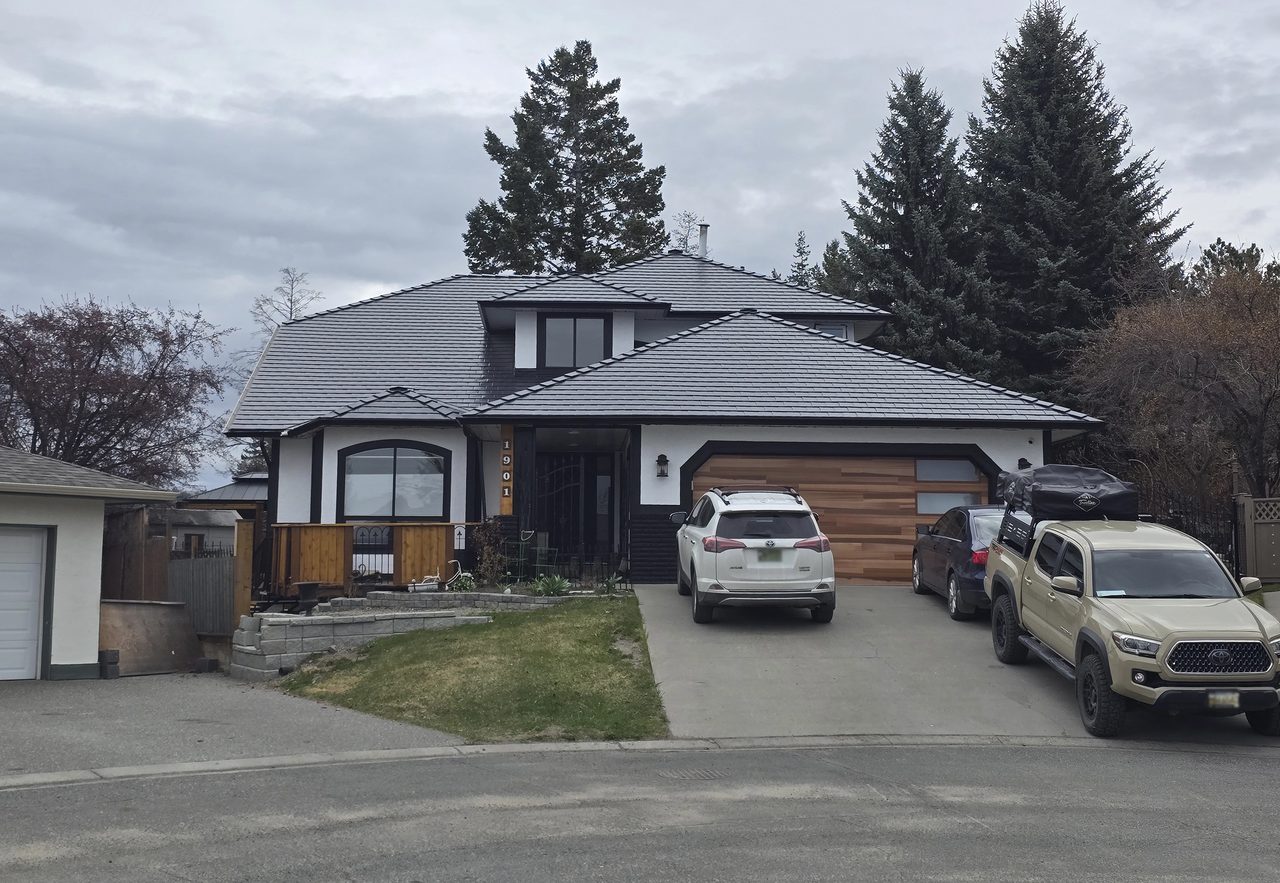 Modern single-family home in Kamloops BC with a complex multi-hip Interlock black aluminum slate roof featuring deep overhangs and cedar-accented garage.