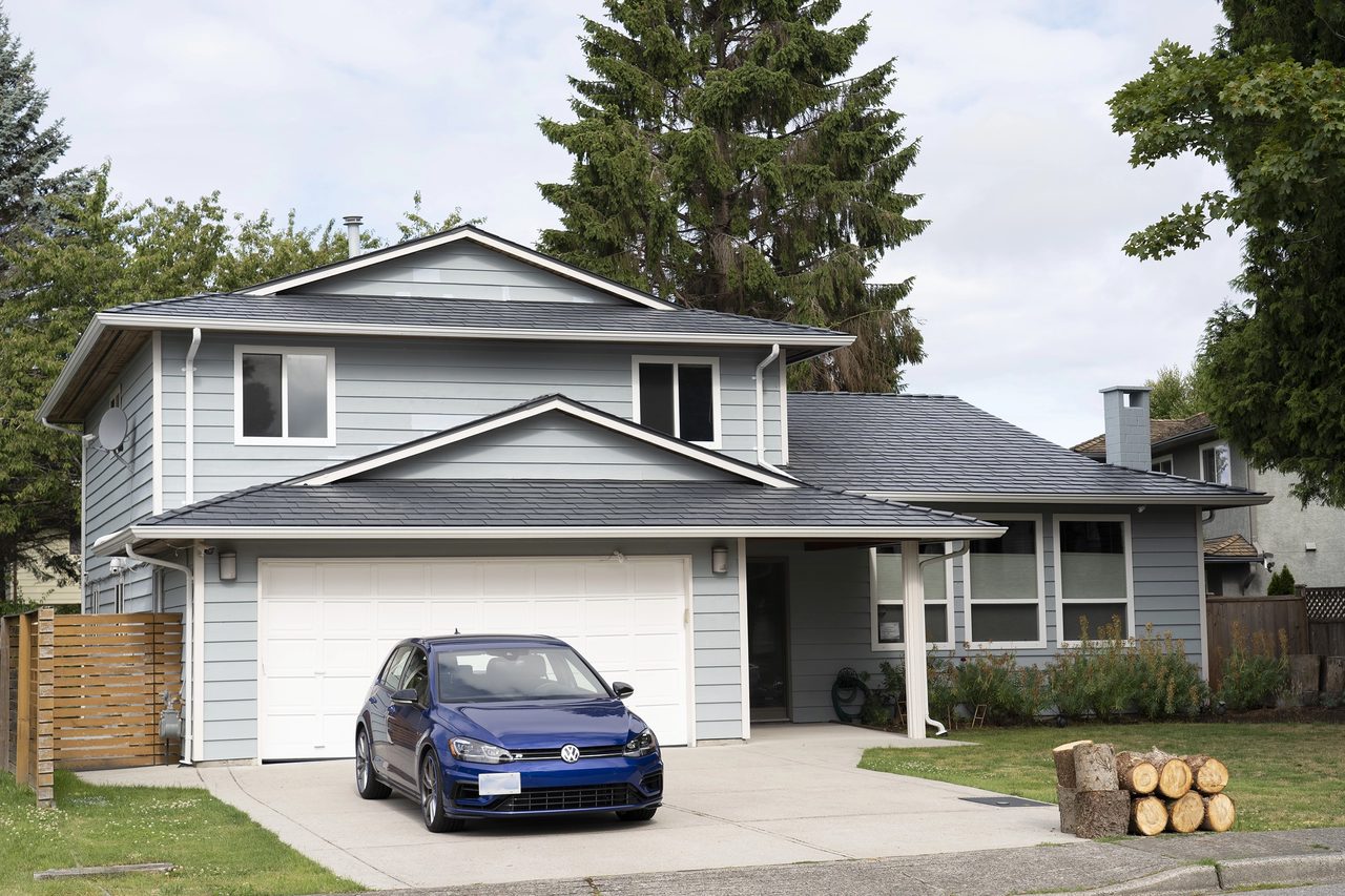 Two-storey suburban home with Interlock deep charcoal aluminum slate metal roofing, multi-plane gable roof, light blue hardie siding, and attached garage in Richmond, BC.