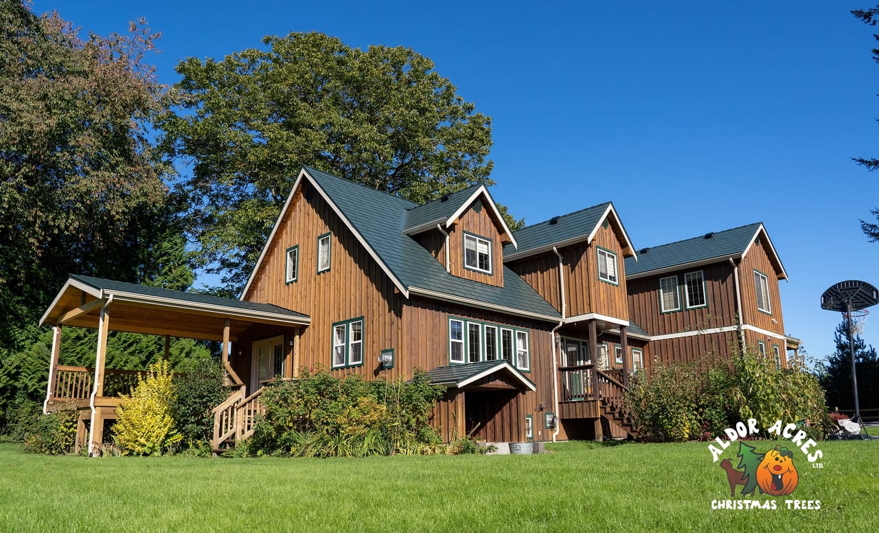 Large two-storey farmhouse with hunter green Interlock aluminum slate metal roofing, multiple dormers, and warm cedar board-and-batten siding in Langley, BC.