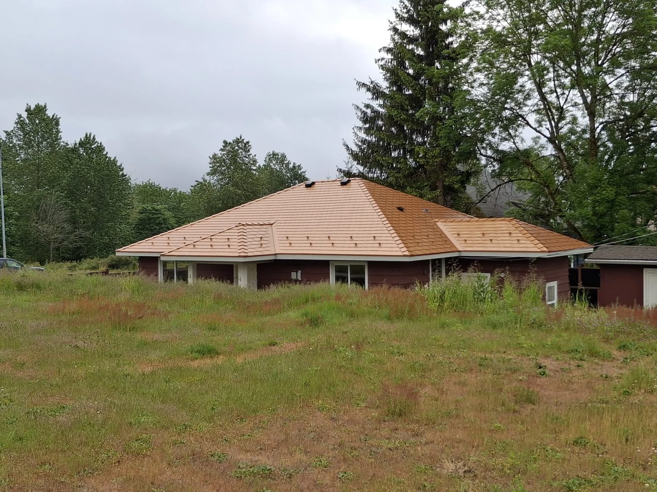 Copper Penny Interlock Slate aluminum roof on a red home with a copper penny metal roof among tall pines, Ladysmith, British Columbia