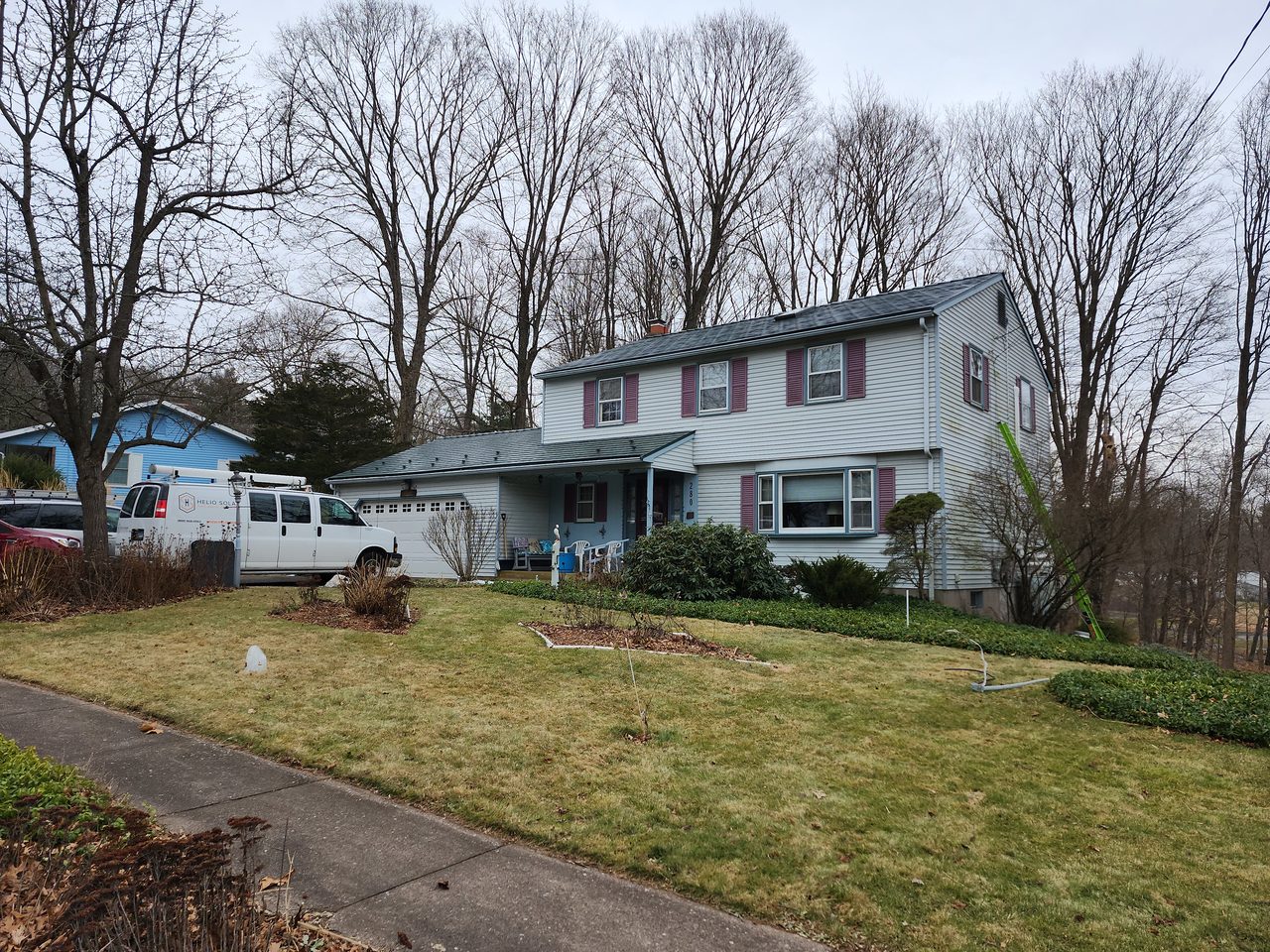 Two-story Colonial home in Manchester, CT with hunter green Interlock aluminum slate metal roof, purple shutters, and chimney, set among bare winter trees.