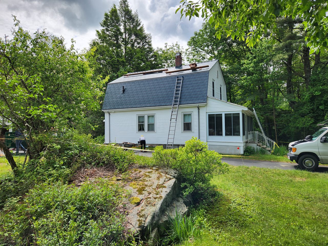 Hunter green Interlock aluminum slate metal roof being installed on a white Cape Cod home with gambrel profile and brick chimney, surrounded by trees in Sharon, MA.