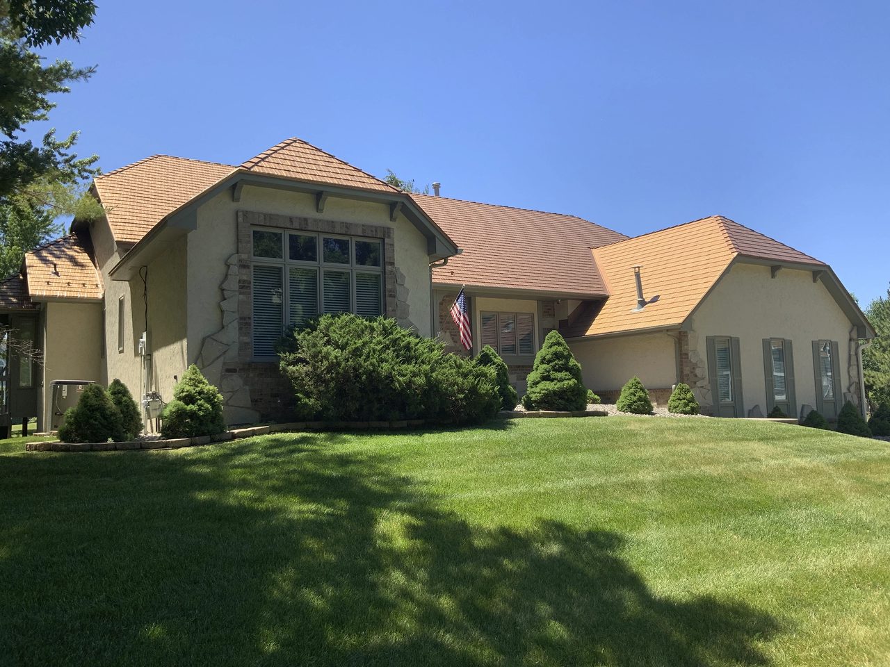 Single-story Tudor-style home in Bloomington MN with Interlock aged-copper cedar-shingle metal roofing across a complex multi-hip roof, stucco exterior, and lush lawn.
