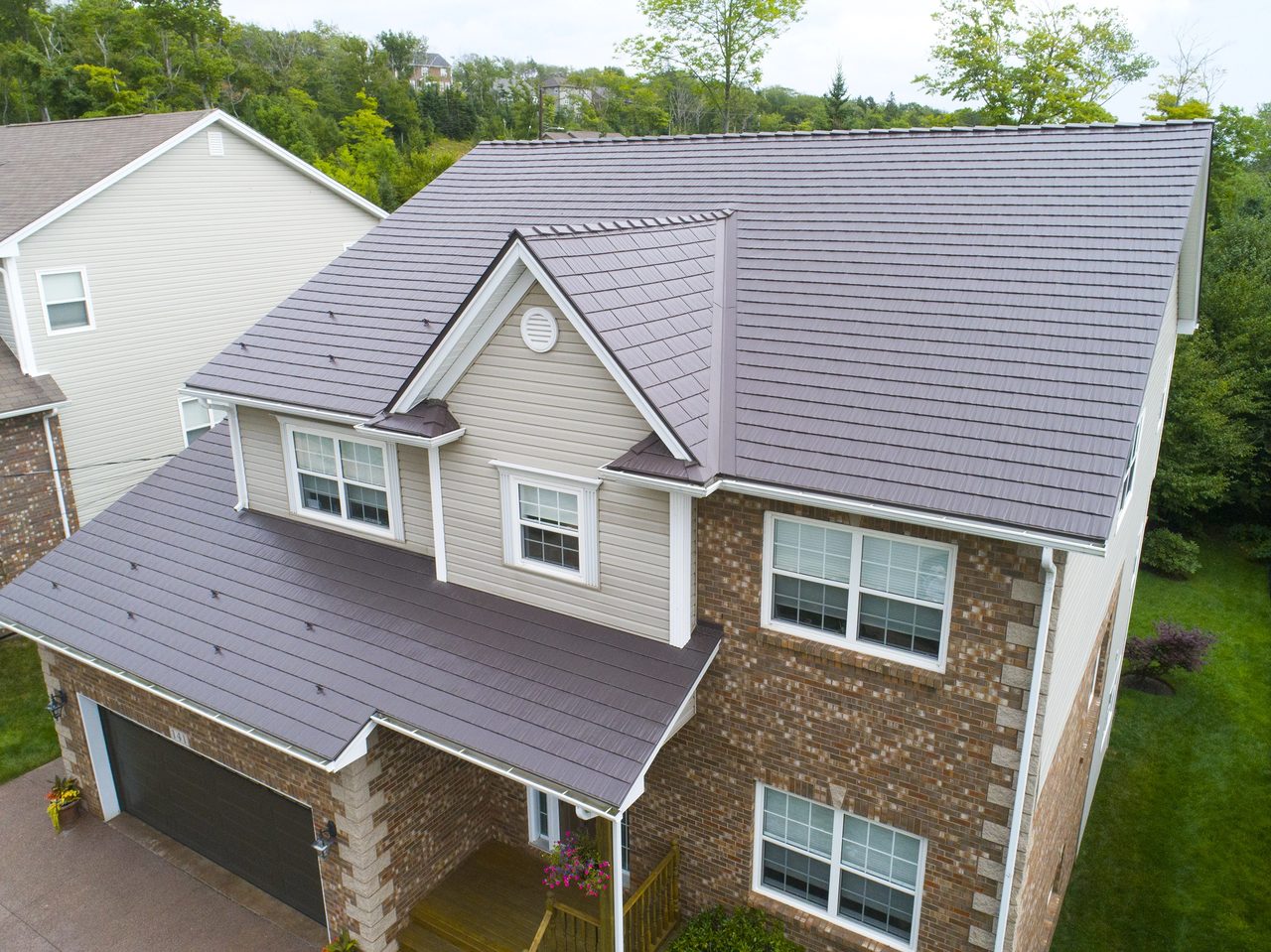 Aerial front-right view of a two-storey brick home in Dartmouth NS with Interlock Tudor Brown cedar shingle metal roofing, featuring a center dormer and covered entry.