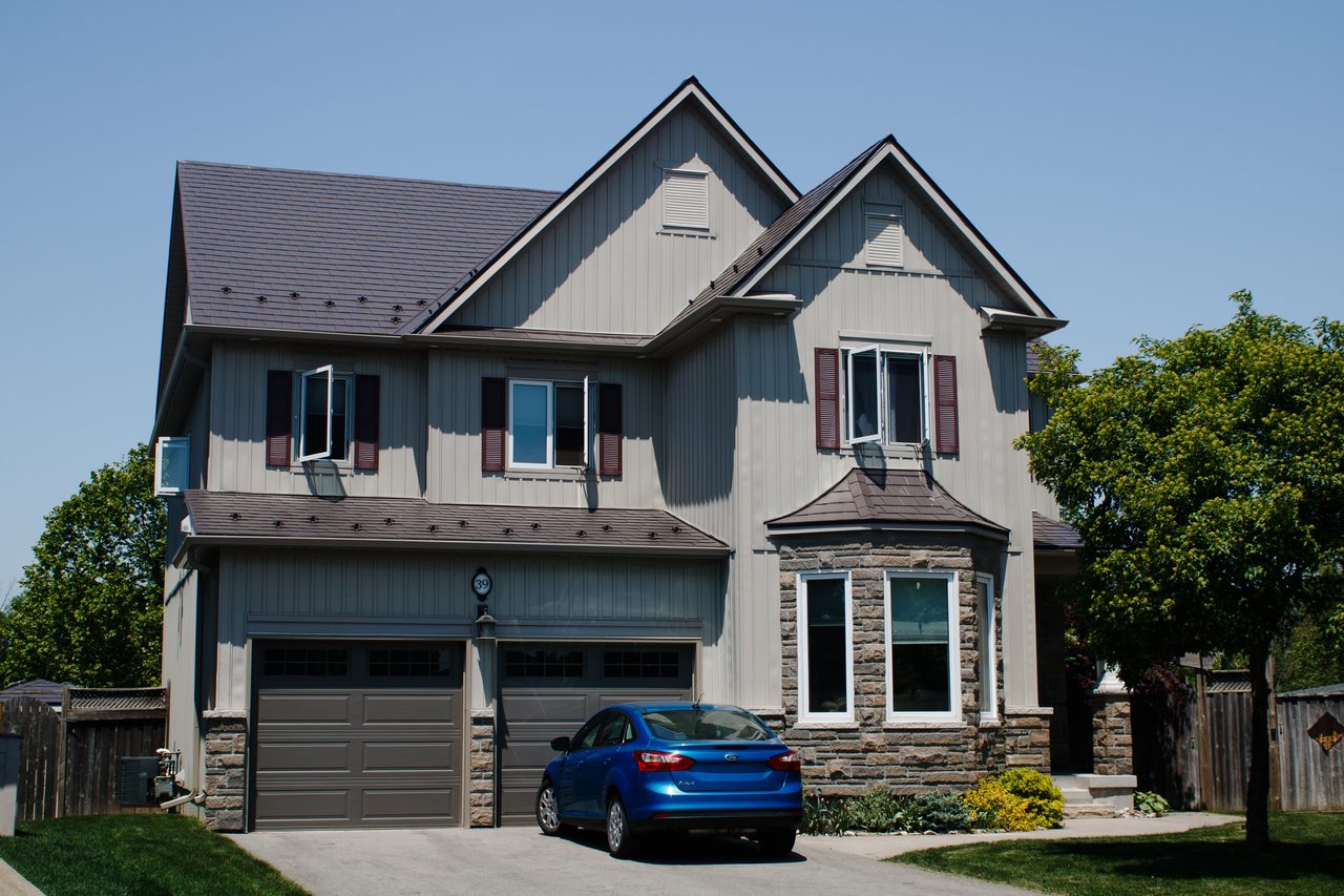 Two-storey Craftsman home in Acton, ON with Interlock Tudor Brown aluminum slate roofing, complex multi-gable roofline, stone accent base, and decorative dormers.