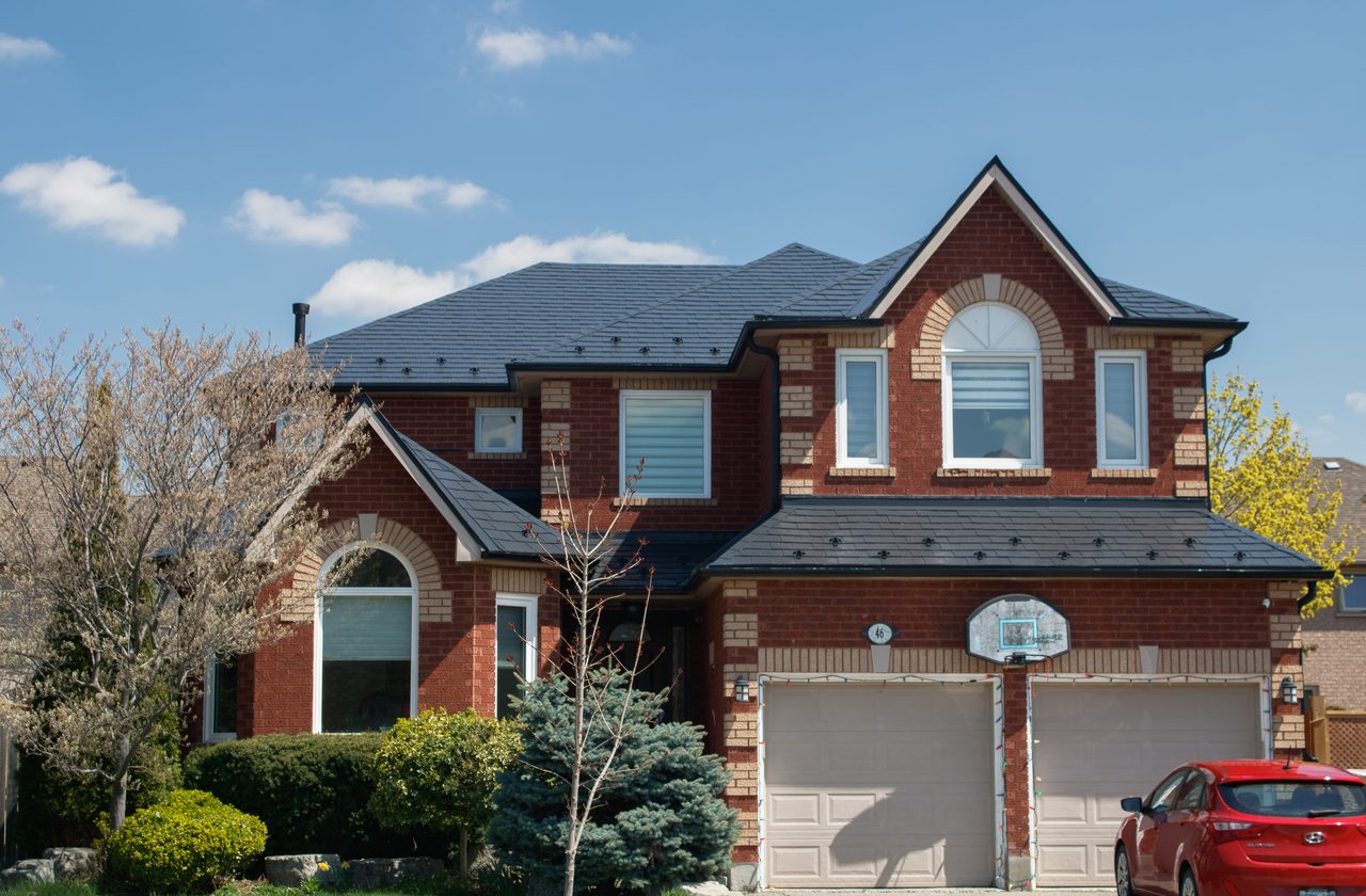 Two-storey red-brick Colonial home in Stoney Creek with complex multi-hip black Interlock aluminum slate metal roof, dormers, and double garage.