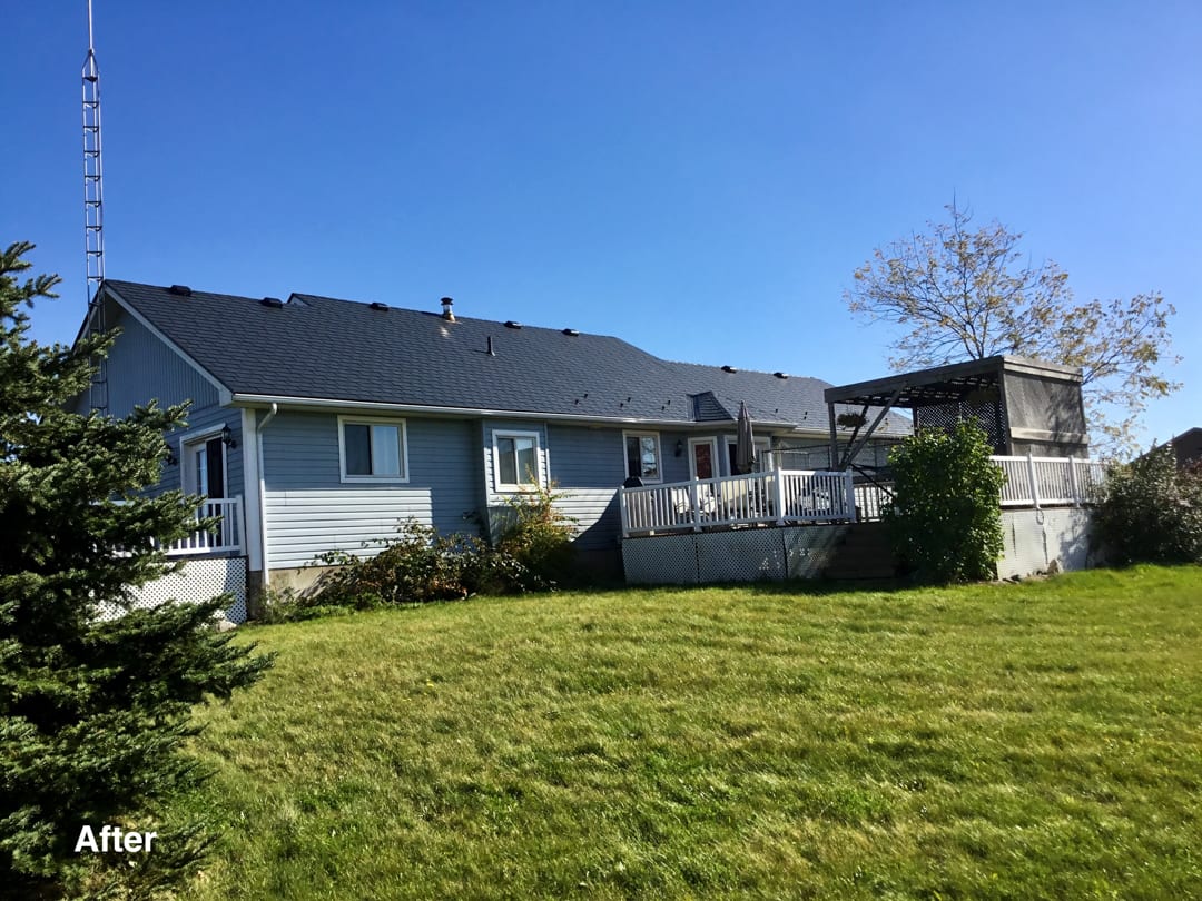 Rear elevation of a ranch-style home in Mount Forest ON featuring a new black Interlock aluminum slate metal roof with white deck railings.