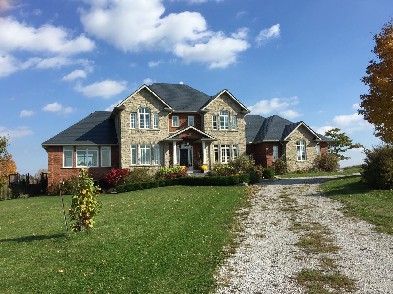Large two-storey Colonial stone-and-brick home in rural Schomberg, ON, featuring a complex multi-hip Interlock aluminum slate roof in Deep Charcoal.