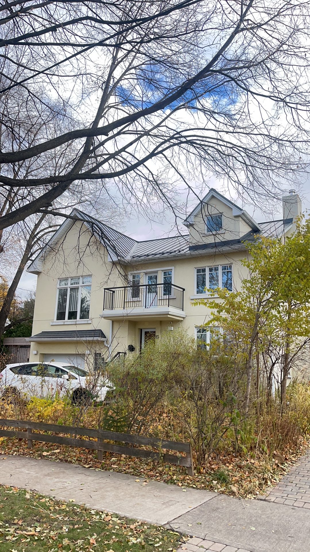 Two-storey Etobicoke home with deep charcoal standing seam metal roof featuring dormers and complex multi-plane roofline, photographed from street in autumn.