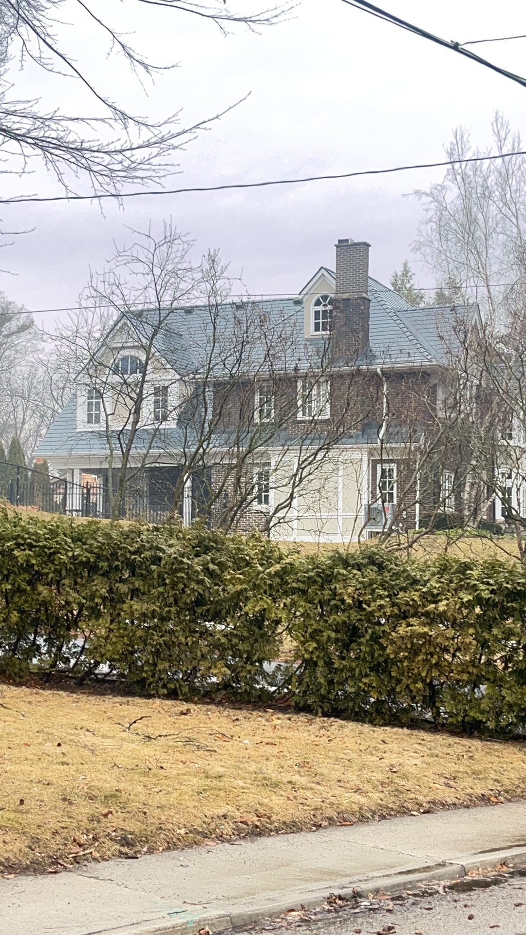Two-storey colonial brick home in Burlington ON with steep deep charcoal Interlock aluminum slate roof, twin dormers, and brick chimney, viewed from street.