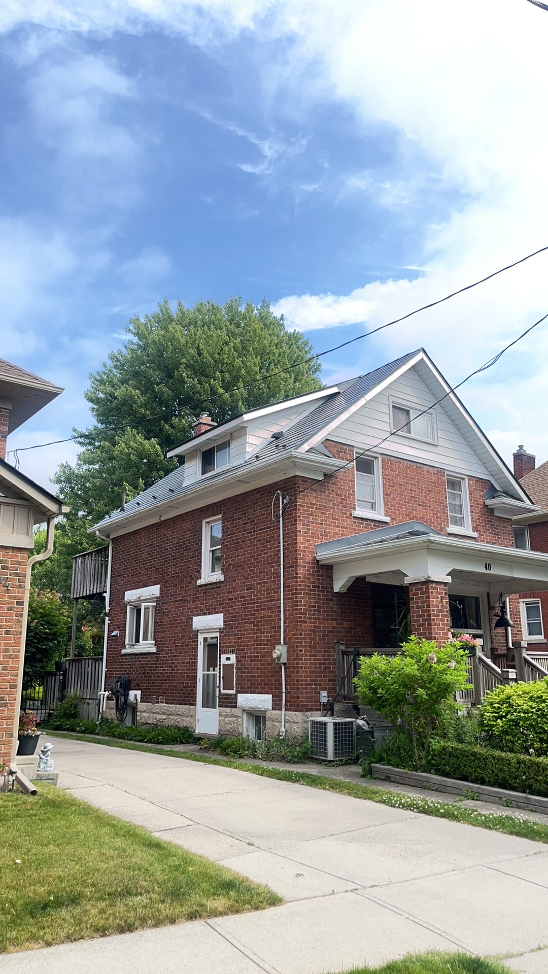 Two-storey red brick home in Kitchener ON featuring Interlock deep charcoal aluminum slate metal roofing with dormer and covered front porch.