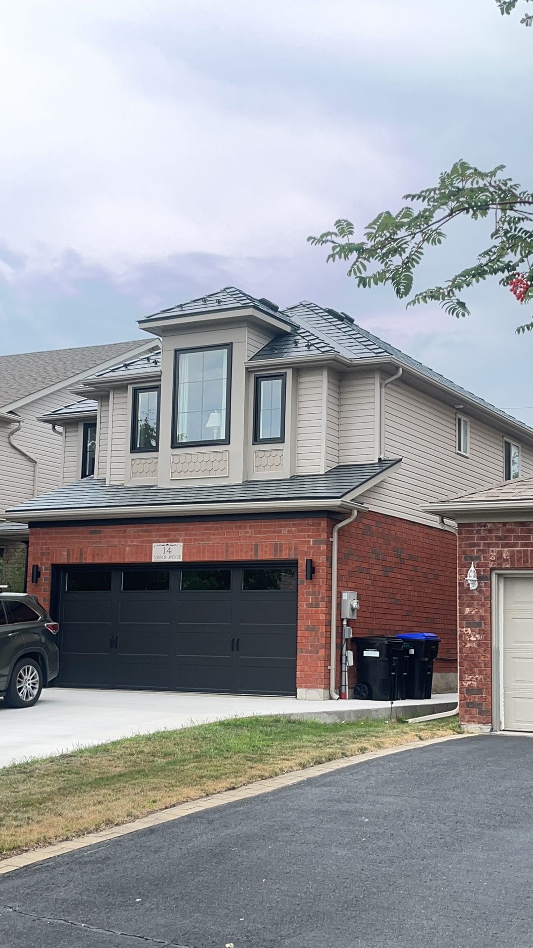 Two-storey brick home in Collingwood ON with Interlock deep charcoal aluminum slate metal roofing featuring a prominent front dormer and multi-hip roof.
