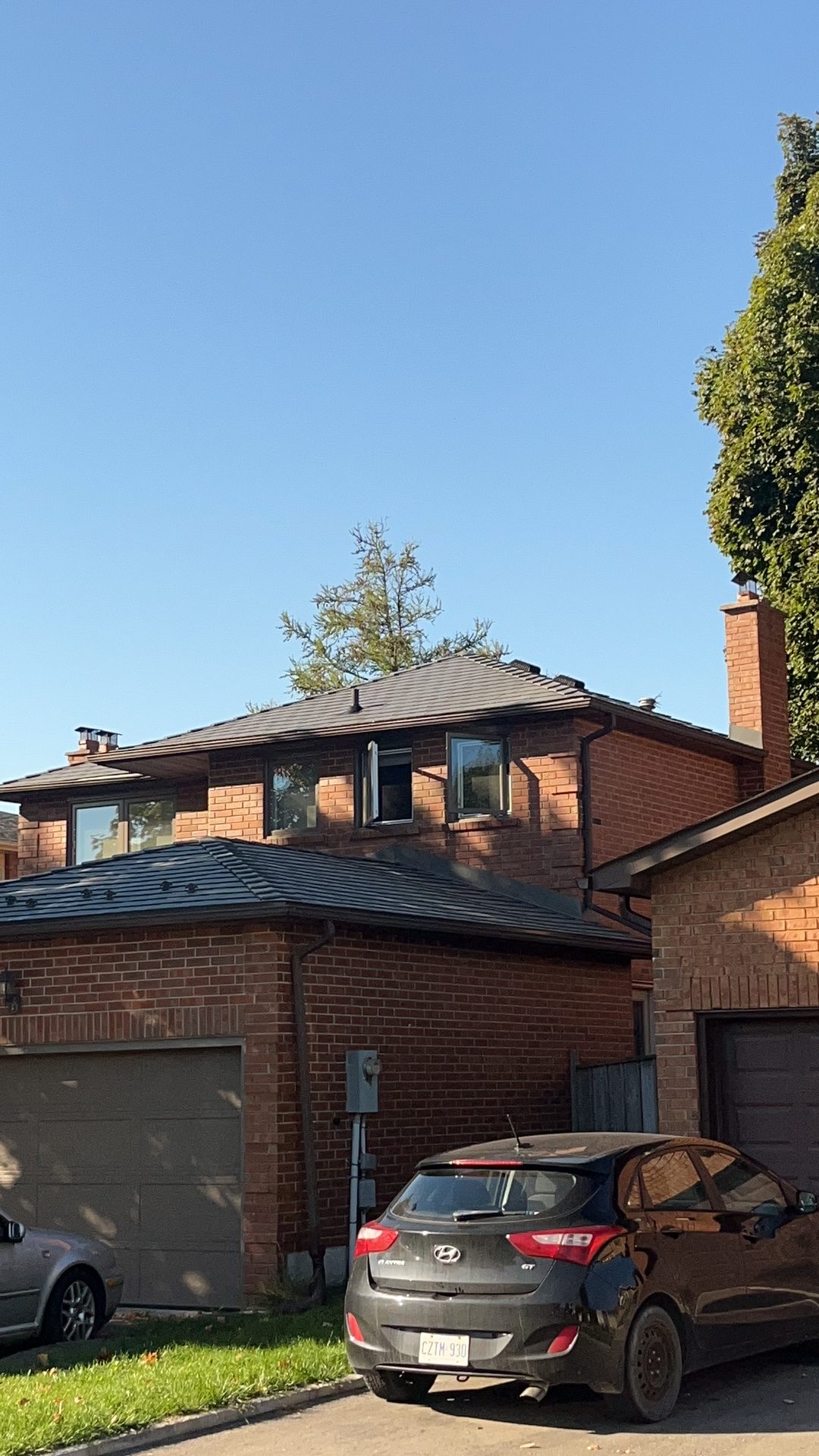 Two-storey red brick home in Markham ON with Interlock Musket Grey aluminum slate multi-hip roof, two chimneys, and attached garage.