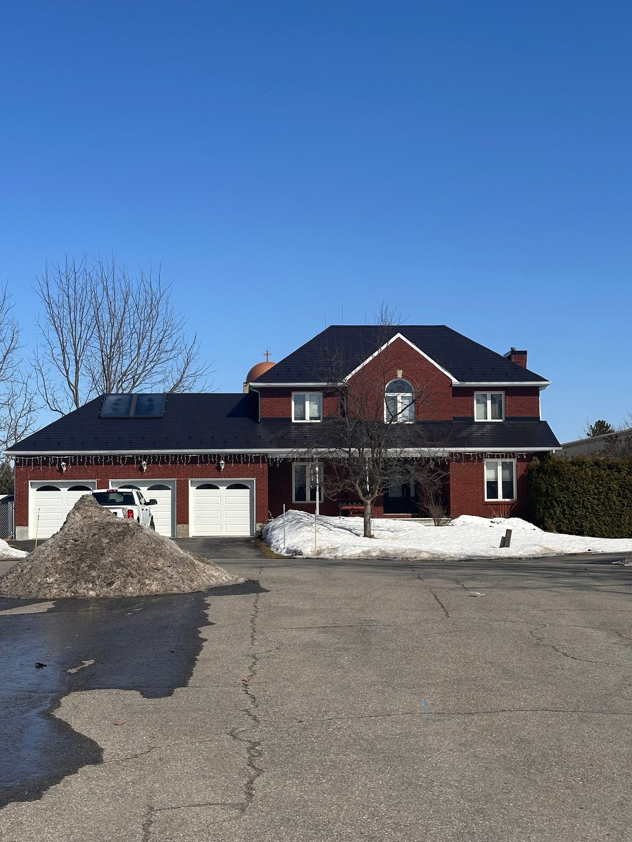 Two-storey red brick Colonial home in Navan ON with black Interlock aluminum slate roofing, turret, skylights, and triple-car garage in winter.